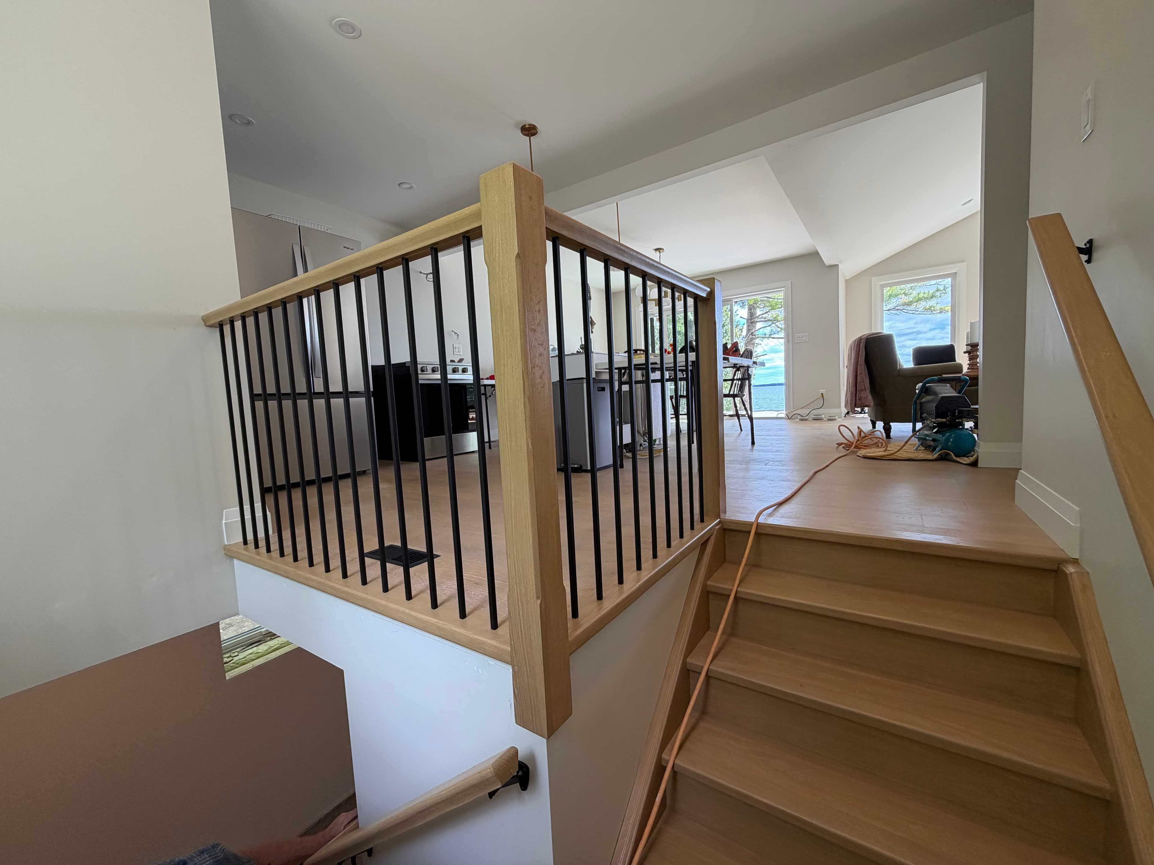 Light wood landing guardrail with black balusters beside a bright lake-facing living area.